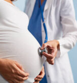 Doctor listening breath of baby in pregnant female abdomen
